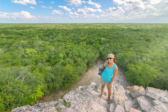 High angle portrait of woman wearing sunglasses and hat while standing on mountain against green landscape