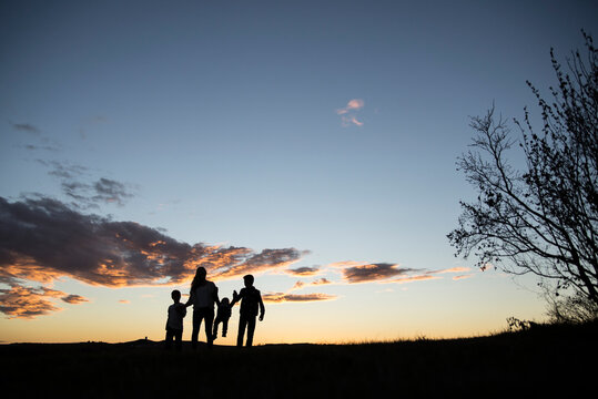 Happy silhouette family standing on field against sky during sunset