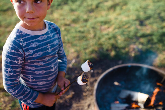 Boy looking away while roasting marshmallows in campfire on field