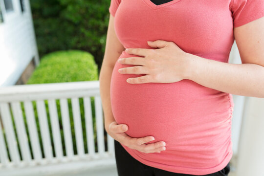 Midsection of pregnant woman touching belly while standing in porch