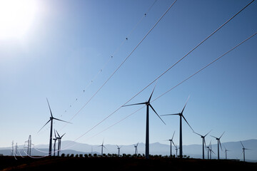 Windmills and electricity pylons on field against clear blue sky during sunny day