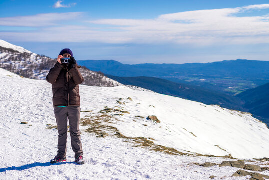 Woman taking photo while standing at snow covered mountain aginst cloudy sky