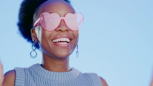Black woman, heart sunglasses and face in studio with wink, choice or happiness for fashion by blue background. Gen z girl, glasses or shades with smile, portrait or happy for accessory by backdrop