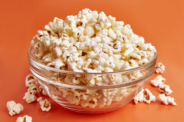 A bowl on an orange background is completely filled with popcorn.
