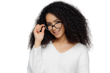 Horizontal shot of satisfied female teacher keeps hand on frame of glasses, smiles happily, has Afro hairstyle, wears casual white jumper, stands indoor over grey background. Good mood and beauty