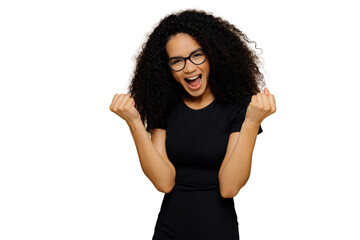 Triumphing lovely dark skinned woman raises clenched fists, yells with joy, celebrates victory,...