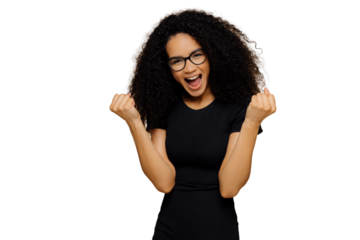 Triumphing lovely dark skinned woman raises clenched fists, yells with joy, celebrates victory, wears black clothing, stands against brown background, feels like winner. Body language, success concept