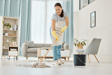 Woman cleaning the floor with a mop in the living room in home with a smile. Happy asian cleaner...