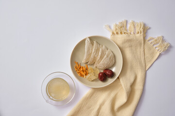 Dish of edible bird’s nest, jujube (ziziphus jujuba), cordyceps (Ophiocordyceps sinensis) and rock sugar, a cup of bird’s nest soup next to it. Healthy combination to enhance skin and health condition