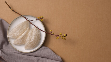 Frame for advertising photo with bird’s nest on white round dishes, flower branch and gray handkerchief on brown background. Bird's nest is an expensive culinary ingredient for health