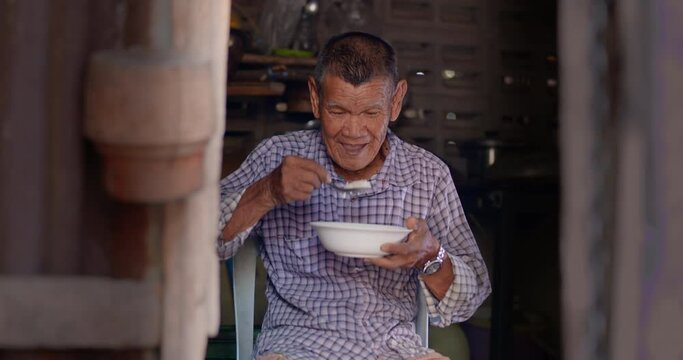 Slow motion of an Asian man who is  a poor elderly native and works as a wage earner in a farm, live in a poor house, eating rice. Use in documentary concept.