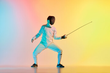 Young man, male fencer with sword practicing in fencing over gradient pink-yellow background in neon light. Sportsman shows fencing technique