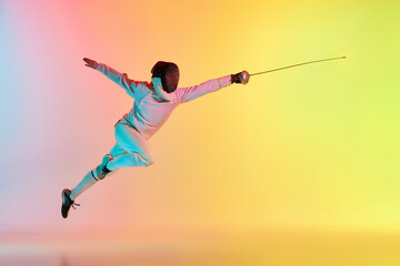 Long attack. Young man, male fencer with sword practicing in fencing over gradient pink-yellow background in neon light. Sportsman shows fencing technique - obrazy, fototapety, plakaty