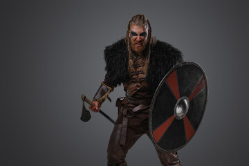 Shot of furious nordic warrior dressed in leather armor and fur against gray background.