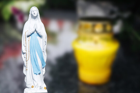 Catholic cemetery background. All saints holiday. Grave candle light. Mother Mary pray. Blessed virgin statue. Yellow grave candle.