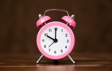 Pink retro alarm clock on brown wooden background, daylight savings time concept