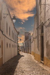 Fototapeta na wymiar The view of narrow paved street of Evora with the cozy white and yellow houses. Evora. Alentejo. Portugal