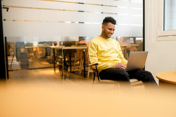 Concentrated determined young freelancer guy sitting in armchair in relaxed pose, typing on laptop, programmer is working on project, developing software, male student websurfing