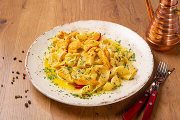 Pappardelle pasta with chicken fillet, garlic and chili sprinkled with parmesan cheese and chopped parsley, close up. The dish is served with cutlery on a wooden table.