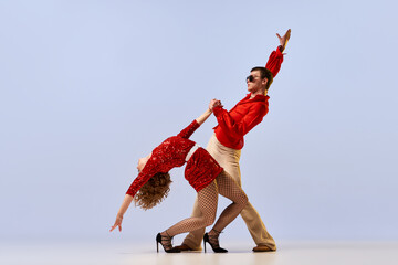 Disco ballroom dances. Expressive couple of dancers in bright retro fashion clothes, stage costumes dancing over lilac color background. Concept of music, art, dance, retro
