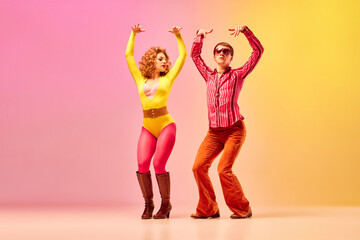 Stylish expressive excited couple of professional dancers in retro style clothes dancing disco dance over pink-yellow background.