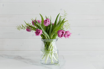 Purple bouquet of tulips on a marble table against a white wooden wall.