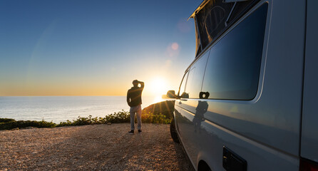 man standing with digital device at his Transporter Camping Van bus at the California Ocean in the...