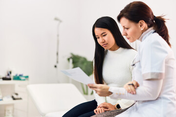 A confident female doctor sitting with an Asian patient, holding a result.