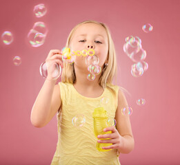 Portrait, fun and girl blowing bubbles, content and playing in studio while posing against pink background. Hand, face and child enjoying freedom, toy and innocent magic while standing isolated