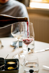 Poring red whine in a glass at a diner table 