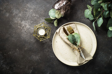 White craft plate, cutlery, wine glass and eucaliptus at black stone table. Top view image.