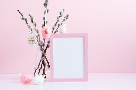 Easter holiday composition. Empty pink photo frame mockup, vase with willow branches, easter eggs, bunny on pink table background. Minimal concept Easter. Front view