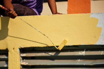 Hand holds paint roller and painting a wall