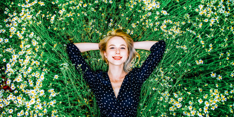 Above view at blonde woman in black dress lying in countryside chamomiles flowers meadow