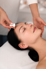 Crop beautician applying serum on clients face