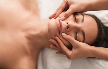 Obraz na płótnie Canvas Crop masseuse doing face massage to client