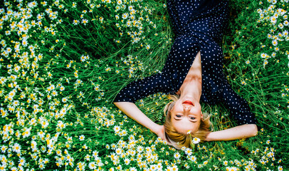 Above view at blonde woman in black dress lying in countryside chamomiles flowers meadow