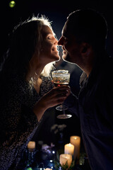 A romantic close-up of an elegant couple holding wine glasses, illuminated with moody backlight and smoke, with candles on the table creating an intimate atmosphere.