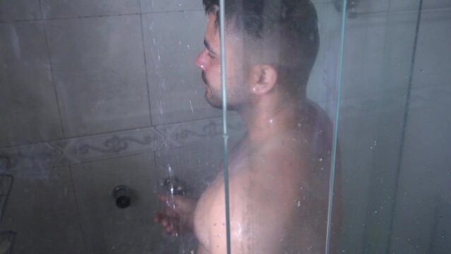 Average man is having a shower. Man completely naked to have a hot shower behind the glass.