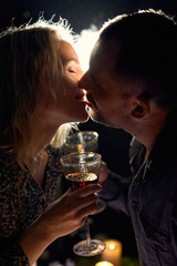 A romantic close-up of an elegant couple holding wine glasses, illuminated with moody backlight and smoke, with candles on the table creating an intimate atmosphere.