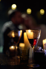Romantic Night Date in Restaurant with Wine and Candles. Back view of couple embracing at a decorated table with burning candles and glasses of red wine.