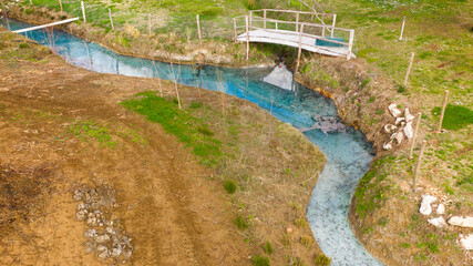 Aerial view on a small stream flowing in the middle of the countryside. The river is clear blue and there is nobody on its banks.
