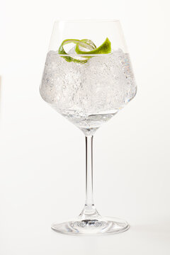 Glass of gin and tonic with lime peel on white background.