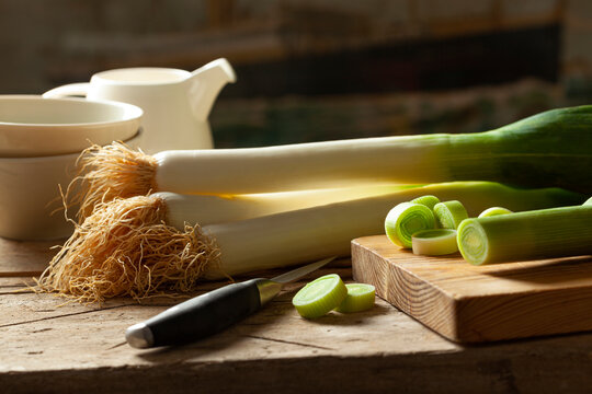 Leeks with roots and sliced on rustic wooden table
