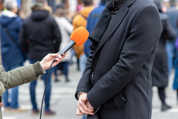 Journalist holding microphone making media interview with male politician or business person. Street interview or vox popoli concept. - obrazy, fototapety, plakaty
