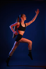 Fototapeta na wymiar Running, conception of sports. Beautiful muscular woman is indoors in the studio with neon lighting