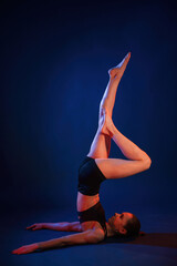 Shoulder stand. Beautiful muscular woman is indoors in the studio with neon lighting