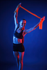 Holding stretching tape in hands. Beautiful muscular woman is indoors in the studio with neon lighting