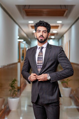 Young indian businessman adjusting coat and standing at office