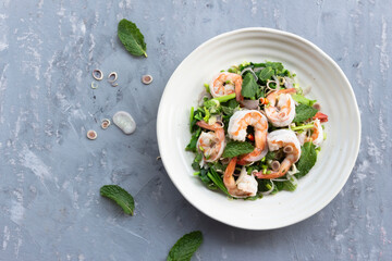 Healthy food shrimp salad has peppermint lemon grass kale in bowl on grey wood background.